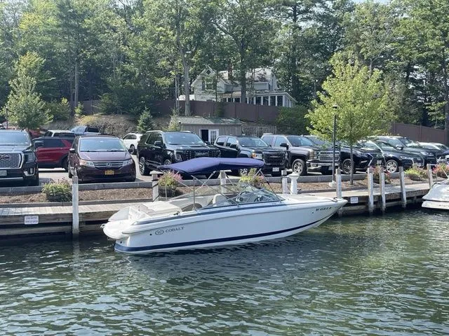 Slide: The Image of 2004 Cobalt 226 boat docked by waterfront with parked cars and trees in the background. - 2