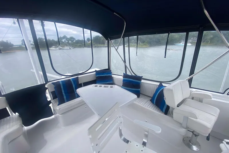 Slide: The Image of 1999 Mainship 430 Trawler interior with seating, table, and blue-striped cushions, overlooking water. - 14