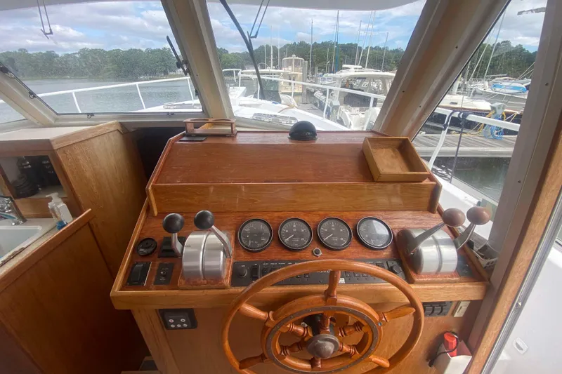 Slide: The Image of 1999 Mainship 430 Trawler helm with wooden steering wheel and control panel, docked at marina. - 22
