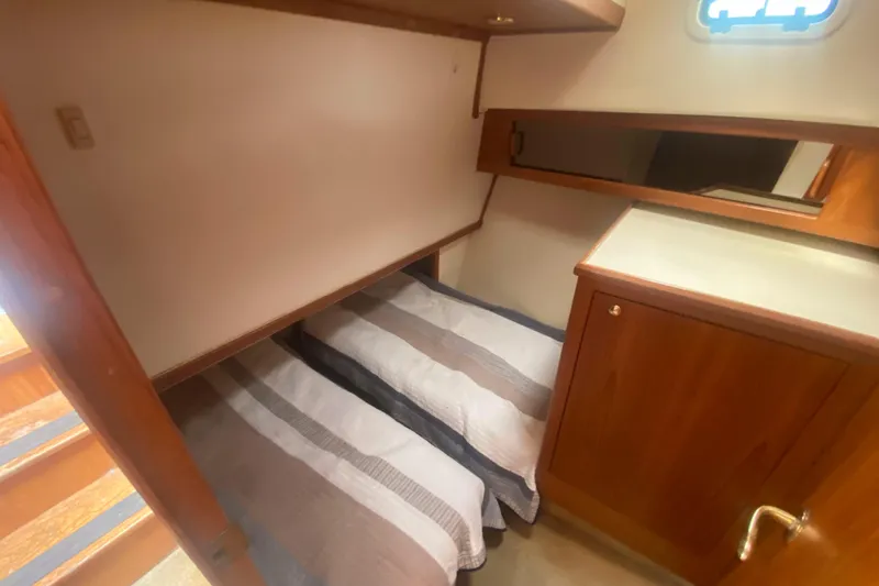 Slide: The Image of 1999 Mainship 430 Trawler cabin with twin beds, wooden cabinetry, and a small window. - 32