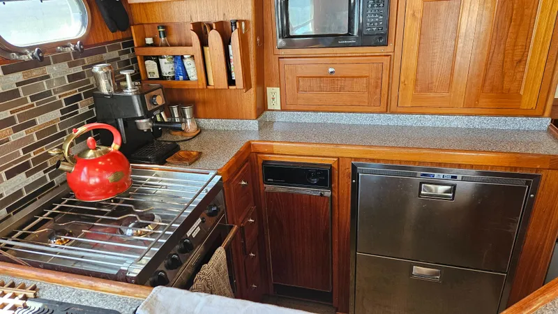 Slide: The Image of 2002 Nordhavn Trawler kitchen with stove, red kettle, microwave, and wooden cabinetry. - 8