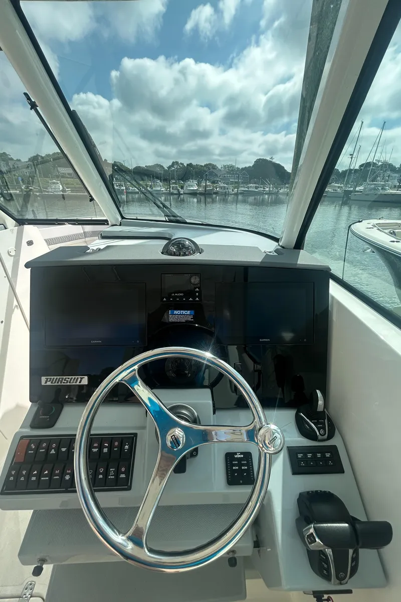 Slide: The Image of 2023 Pursuit DC326 boat interior with cushioned seating and table, docked at marina. - 14