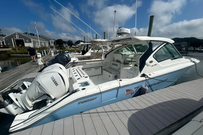 Slide: The Image of 2023 Pursuit DC326 boat docked, featuring sleek design and spacious seating under a clear blue sky. - 8