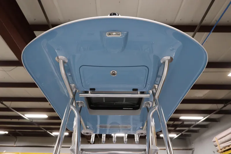 Slide: The Image of 2024 SeaCraft 23CC boat's blue T-top with stainless steel supports in a warehouse. - 48
