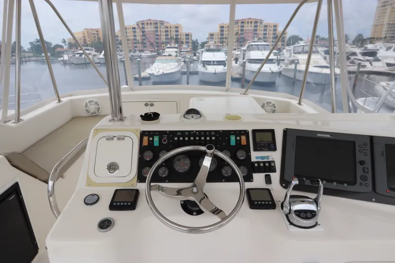 Slide: The Image of The cockpit of a 2001 Riviera 43 Open Flybridge with steering wheel, instruments, and marina view. - 24