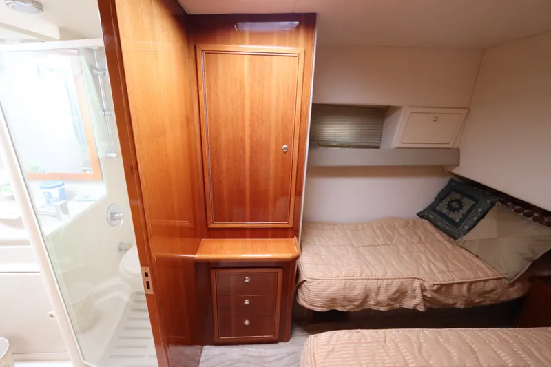 Slide: The Image of The cabin of a 2001 Riviera 43 Open Flybridge features two single beds and a wooden cabinet. - 49