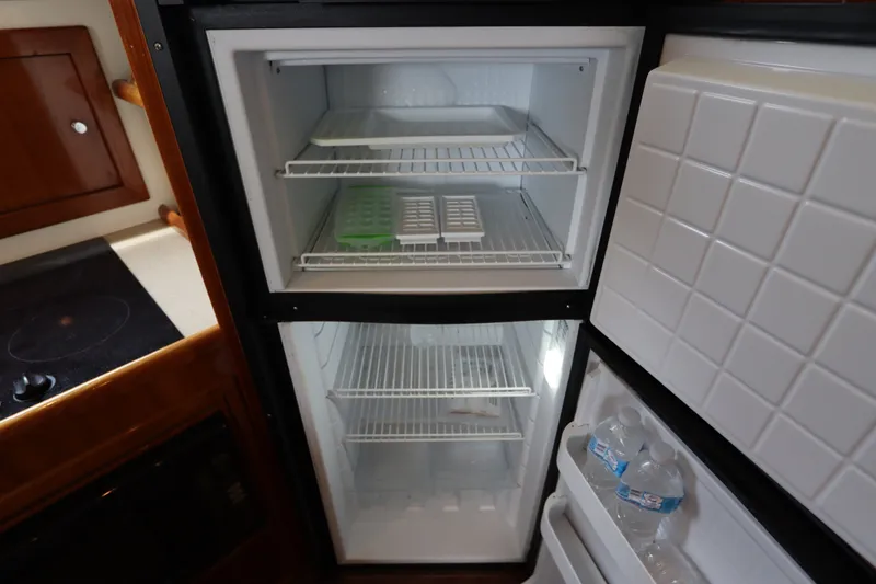 Slide: The Image of A refrigerator with an open freezer showing ice trays and water bottles. Wooden cabinetry is visible. - 45