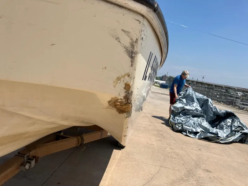 Slide: The Image of 1976 Glastron 156 Open Bow boat with hull damage, person handling tarp nearby. - 13