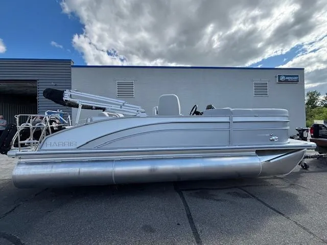 Slide: The Image of 2025 Harris Cruiser 210 pontoon boat parked outdoors under cloudy sky. - 2