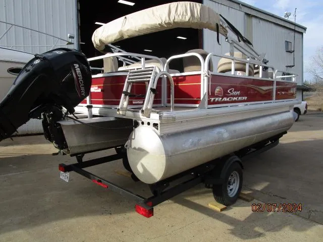 Slide: The Image of 2023 Sun Tracker Bass Buggy pontoon boat on trailer, parked outside a warehouse. - 3