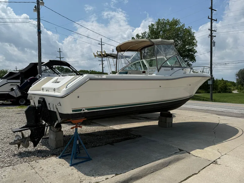 Slide: The Image of 1996 Pursuit 2460 Denali boat on stands, outdoor setting, partly cloudy sky. - 3