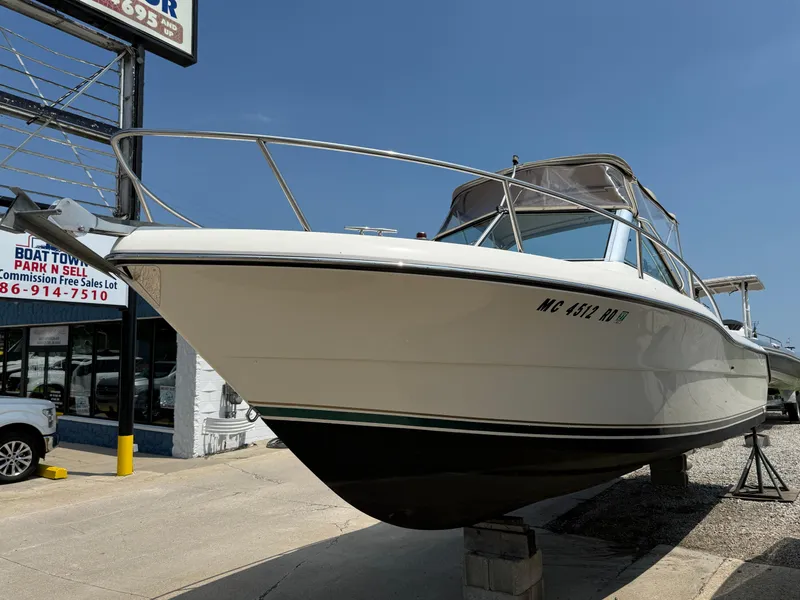 Slide: The Image of 1996 Pursuit 2460 Denali boat displayed at a sales lot under clear blue skies. - 7