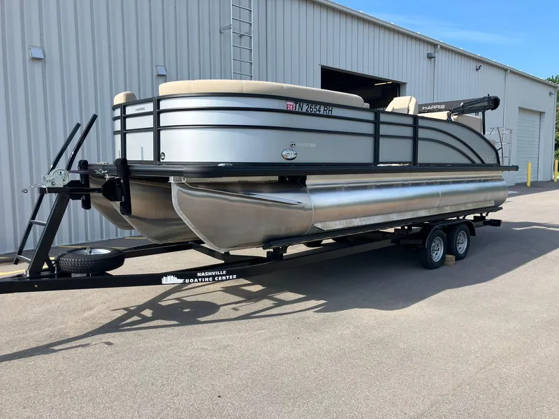 The Image of 2025 Harris Cruiser 230 pontoon boat on trailer, parked outside a building. - 0