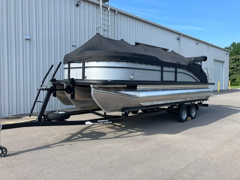 Slide: The Image of 2025 Harris Cruiser 230 pontoon boat on trailer, covered, parked outside a warehouse. - 5
