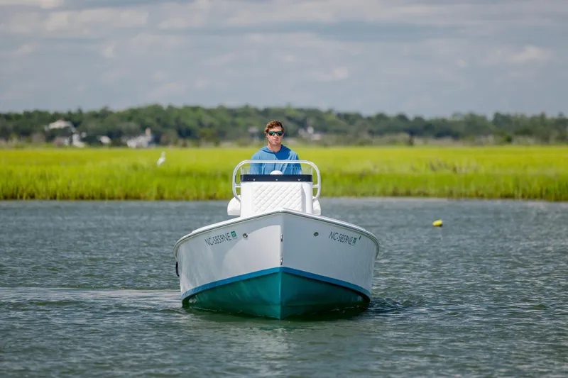 Slide: The Image of Man piloting 2025 Spanish Wells 21 boat on calm water with grassy shoreline. - 2