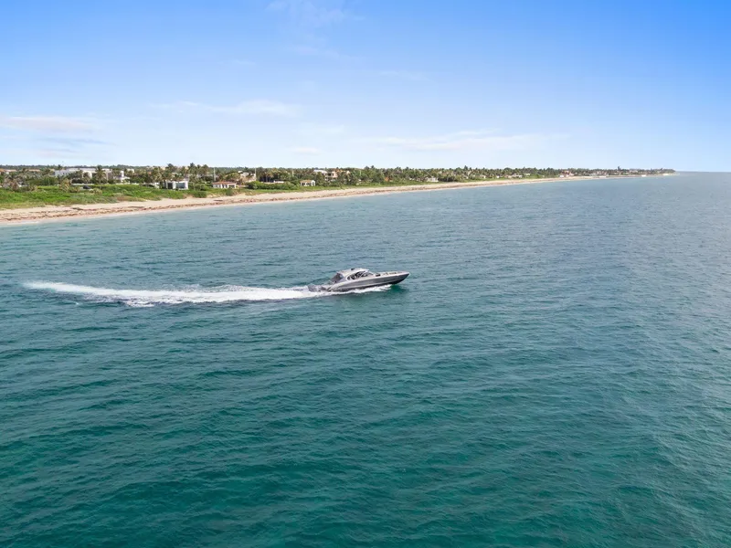 Slide: The Image of 2024 Mystic Powerboats M5200 cruising along a scenic coastline under a clear blue sky. - 36