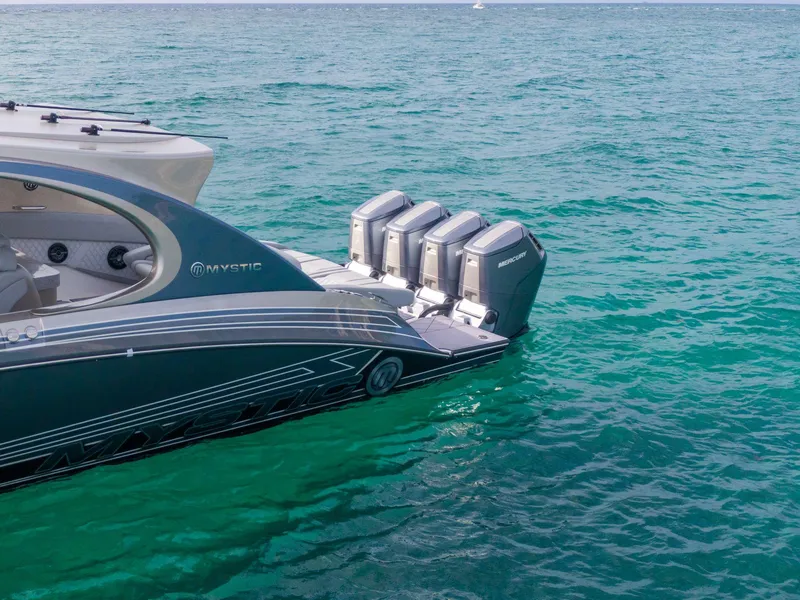 Slide: The Image of 2024 Mystic Powerboats M5200 with quad Mercury engines on turquoise water. - 5