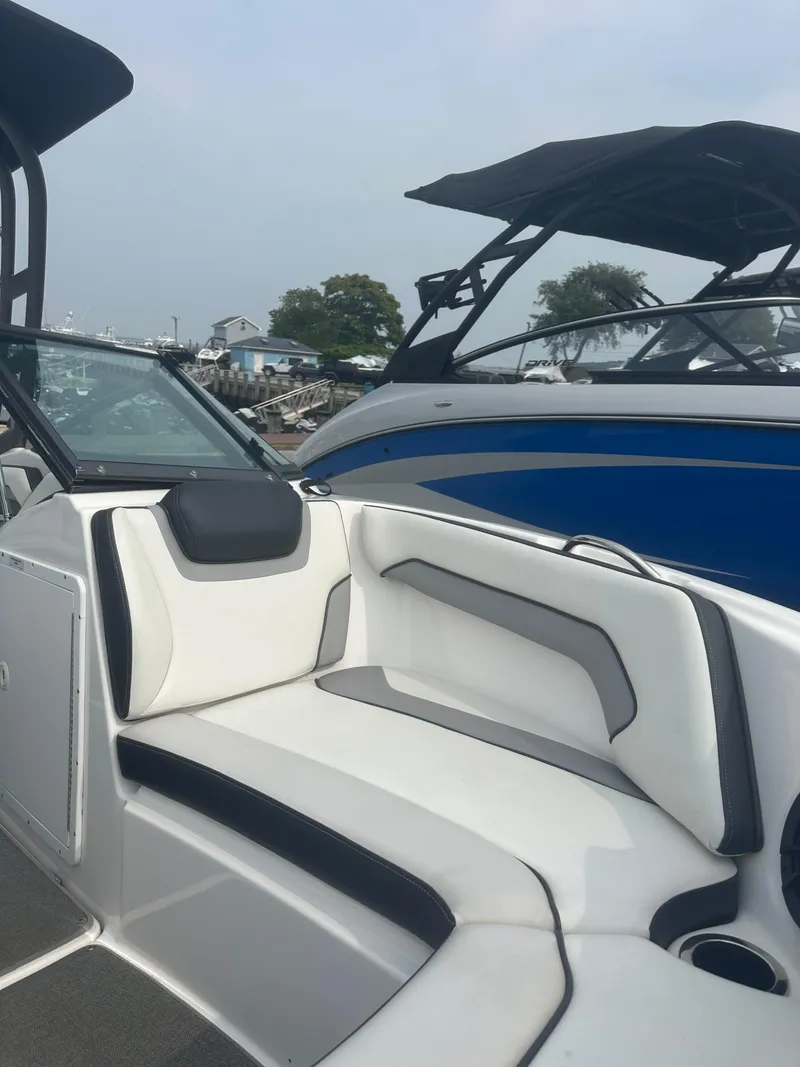 Slide: The Image of 2018 Yamaha Boats AR195 interior with white and black seating, docked beside another boat. - 10