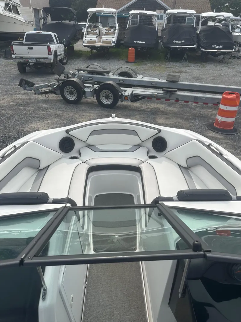 Slide: The Image of 2018 Yamaha AR195 boat interior with seating and windshield, parked near trailers and other boats. - 11