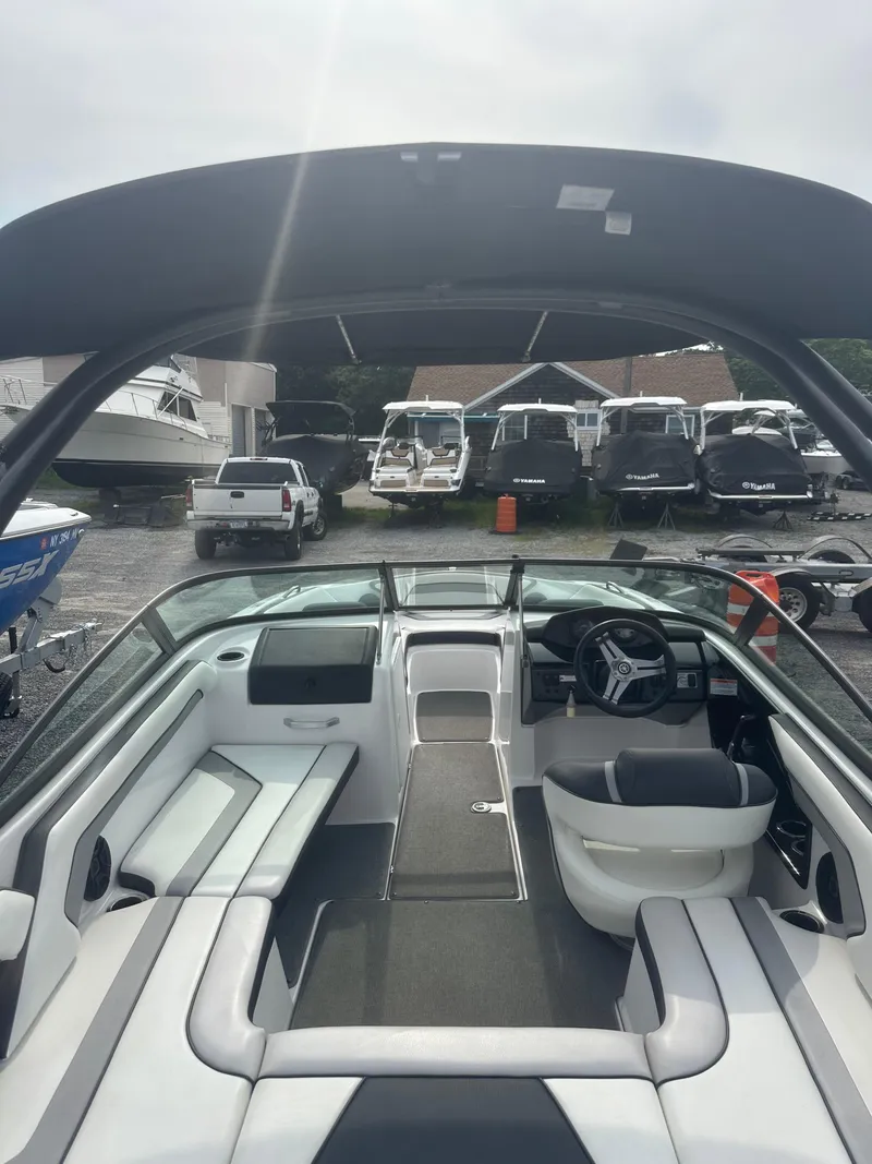 Slide: The Image of 2018 Yamaha Boats AR195 interior with seating and steering wheel, parked among other boats. - 16