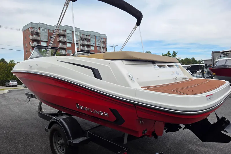 Slide: The Image of 2024 Bayliner VR5 Bowrider I/O boat with red hull on trailer, urban background. - 6