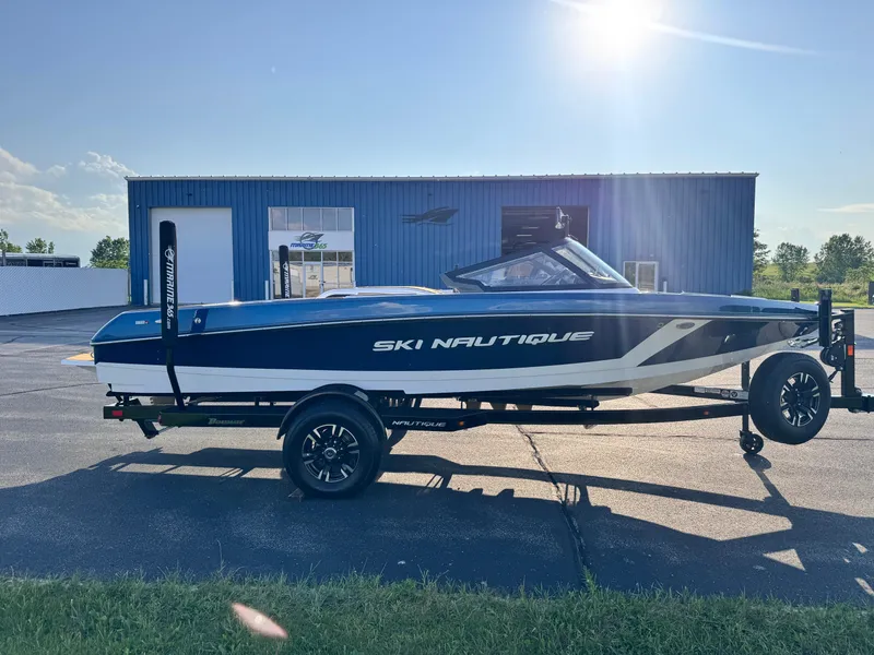 Slide: The Image of 2025 Nautique Ski 200 boat on trailer, parked outdoors under clear sky. - 2