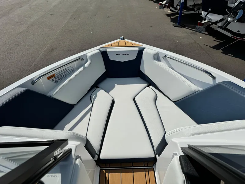 Slide: The Image of 2025 Nautique Ski 200 boat interior with white and blue seating, docked outdoors. - 32