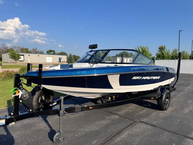 Slide: The Image of 2025 Nautique Ski 200 boat on trailer, parked outdoors under clear sky. - 6