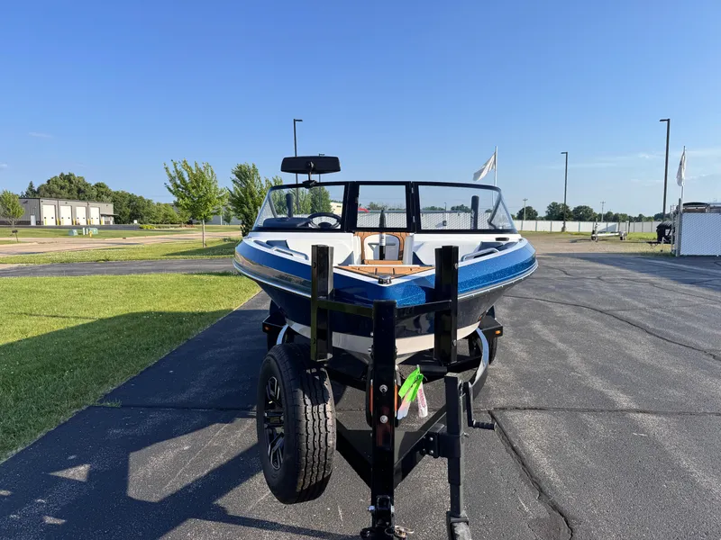 Slide: The Image of 2025 Nautique Ski 200 boat on trailer, parked outdoors on sunny day. - 7