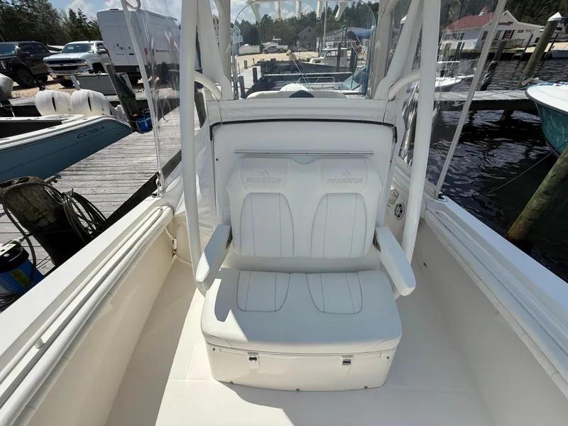 Slide: The Image of 2018 Regulator 23 boat interior with white seating at a marina dock. - 19