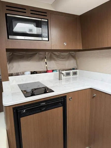Slide: The Image of 2019 Sea Ray 350 Sundancer Coupe kitchen with microwave, stove, and wooden cabinetry. - 17