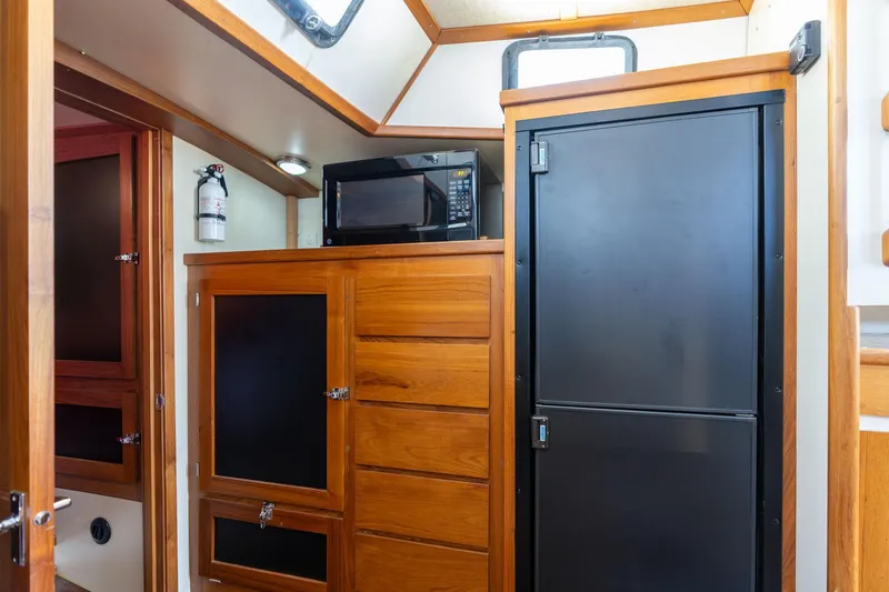 Slide: The Image of 1978 Cascade High Side interior with wooden cabinets, black fridge, and microwave. - 24