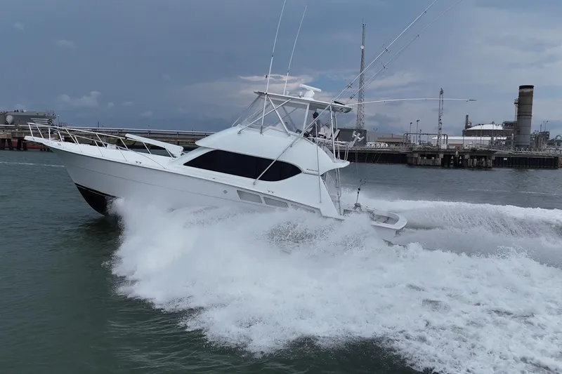 The Image of 2002 Hatteras 50 Convertible Sportfish cruising swiftly in open water near industrial docks. - 0