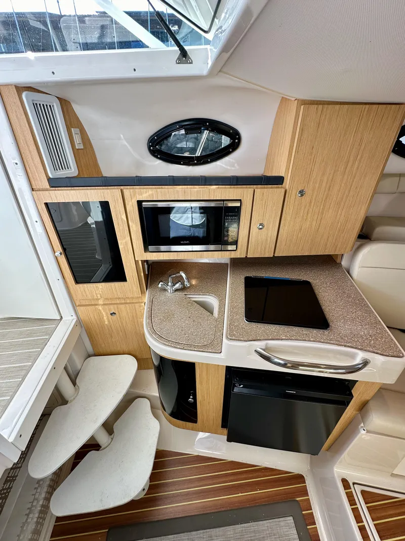 Slide: The Image of 2018 Wellcraft 290 Coastal boat interior with kitchenette, featuring microwave, sink, and compact fridge. - 28