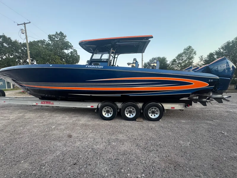 Slide: The Image of 2023 Fountain 38 SC boat on trailer, blue with orange accents, parked outdoors. - 18
