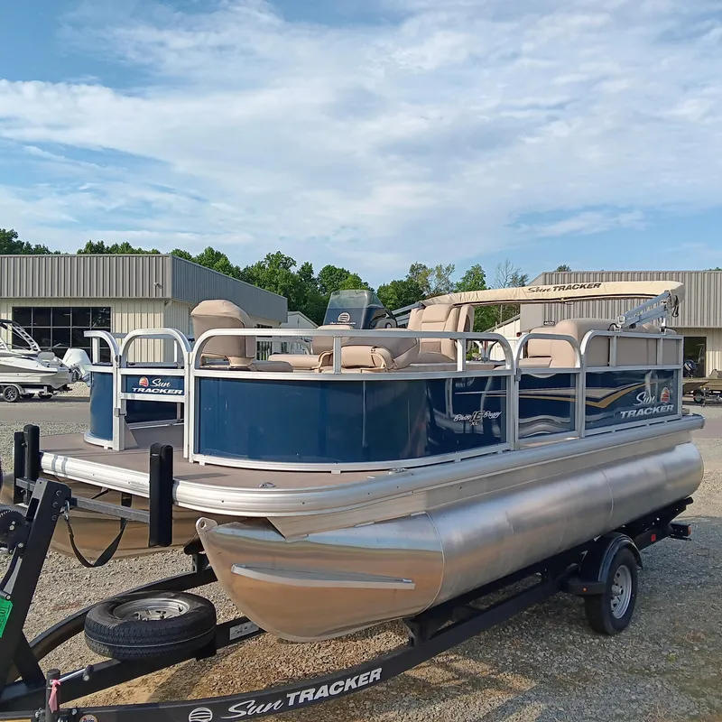 Slide: The Image of 2025 Sun Tracker Bass Buggy 16 XL Select pontoon boat on trailer, outdoor dealership setting. - 3