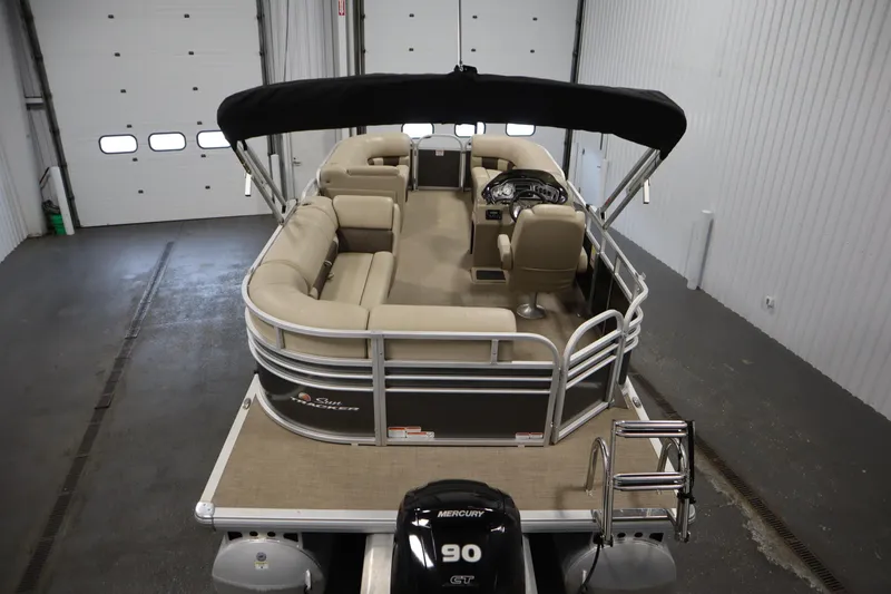 Slide: The Image of 2023 Tracker 20 DLX PARTY BARGE pontoon boat with seating and canopy in a garage. - 10