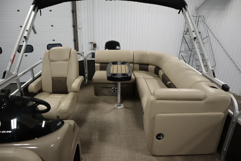 Slide: The Image of 2023 Tracker 20 DLX PARTY BARGE interior with beige seating and table in a showroom. - 32