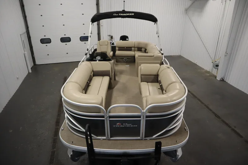 Slide: The Image of 2023 Tracker 20 DLX PARTY BARGE pontoon boat with beige seating in a garage. - 9