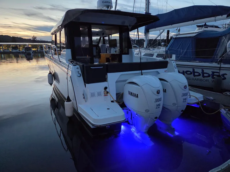 Slide: The Image of 2023 Jeanneau NC Weekender 1095 with Yamaha engines, docked at sunset with blue underwater lights. - 2