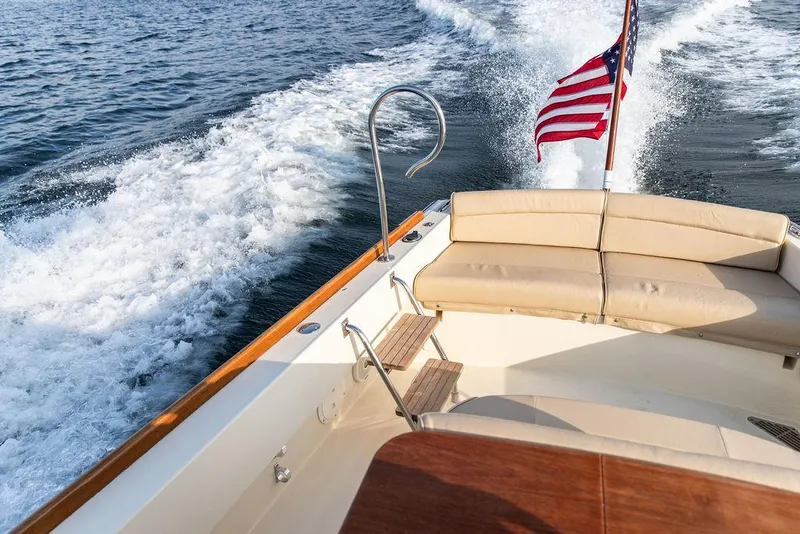 Slide: The Image of 2014 Hinckley T29 CC boat cruising with American flag, beige seating, and ocean wake. - 31
