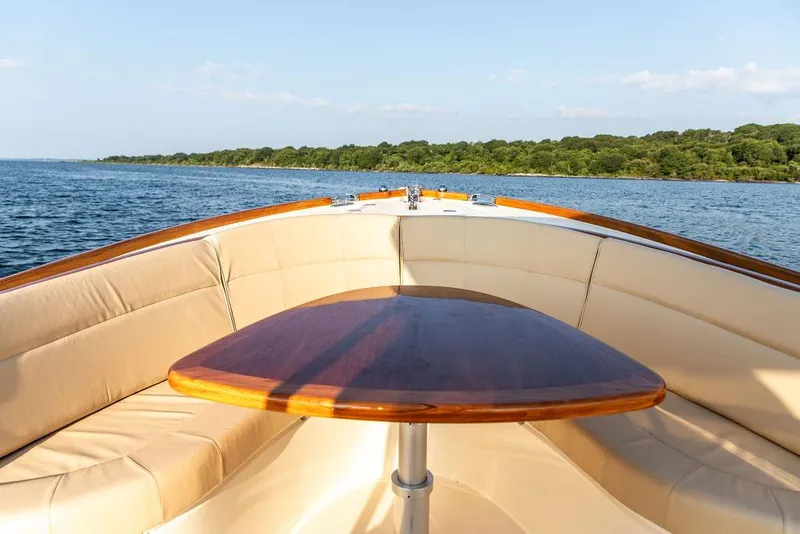 Slide: The Image of Hinckley T29 CC 2014 boat interior with cushioned seating and wooden table on calm water. - 40
