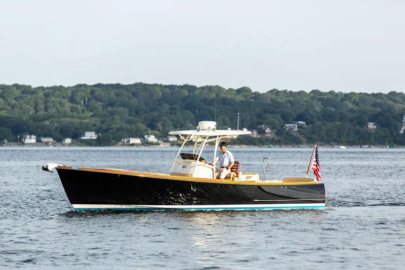 Slide: The Image of 2014 Hinckley T29 CC boat cruising on calm water with forested shoreline in background. - 6