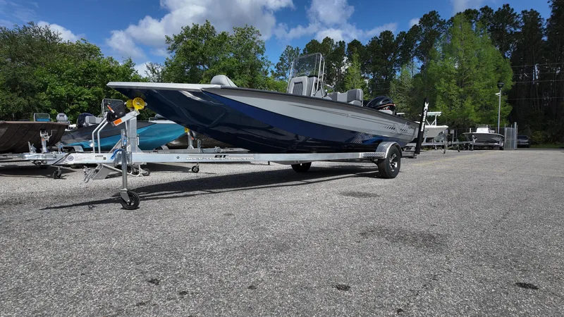 Slide: The Image of 2026 Xpress H20B boat on trailer in outdoor lot, surrounded by trees and blue sky. - 2