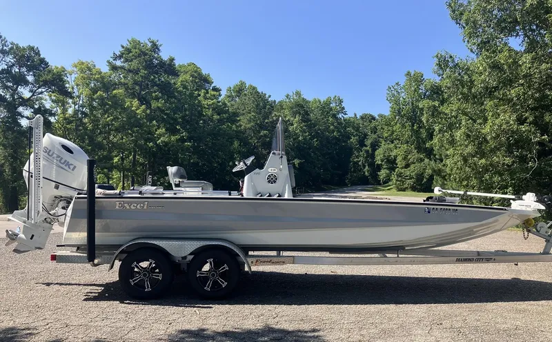 Slide: The Image of 2022 Excel 220 Bay Pro boat on trailer, parked outdoors with trees in background. - 2