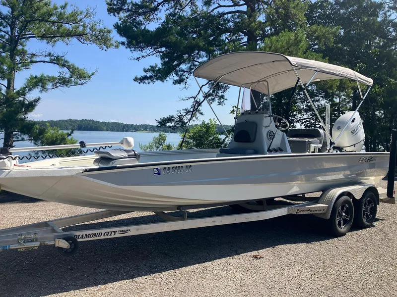 Slide: The Image of 2022 Excel 220 Bay Pro boat on trailer by a lake, surrounded by trees. - 22