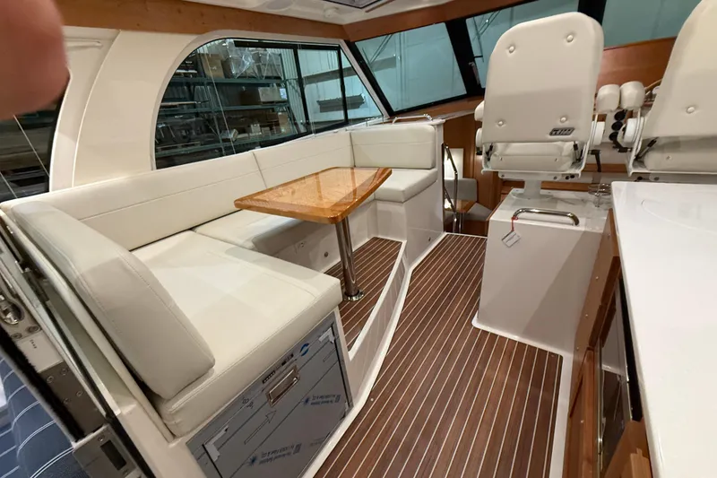 Slide: The Image of 2026 Back Cove 39O yacht interior with white seating, wooden table, and helm chairs. - 17