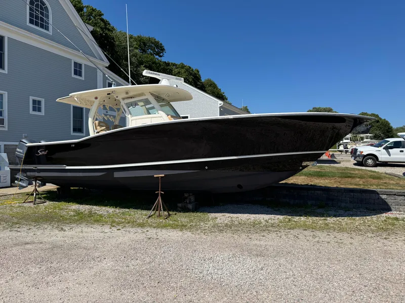 Slide: The Image of 2011 Scout 345 XSF boat on land, black hull, near a building, clear sky. - 2