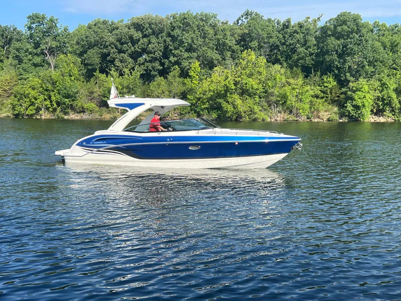 The Image of 2023 Formula 310 Bowrider I/O cruising on a serene lake with lush green trees. - 1