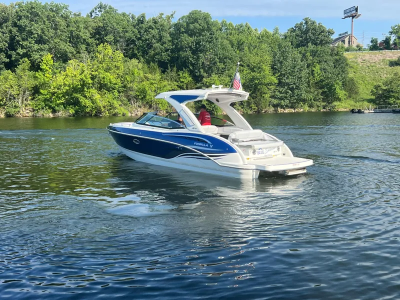 Slide: The Image of 2023 Formula 310 Bowrider I/O cruising on a scenic lake with lush green trees. - 23